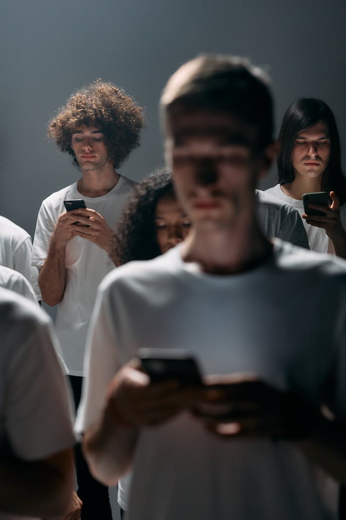 A diverse group of adults absorbed in their smartphones in a dimly lit room, illustrating modern social isolation.